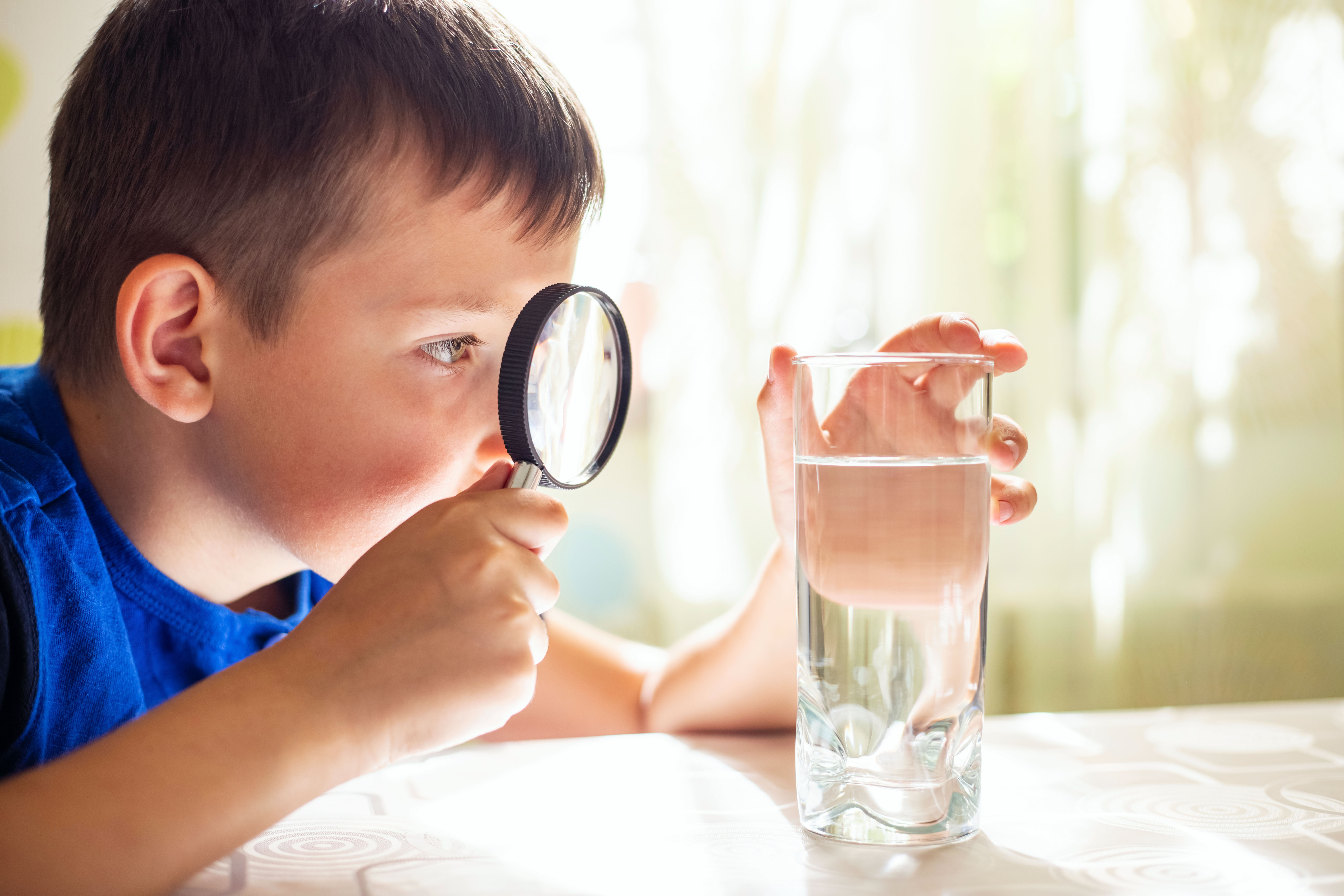 Little boy examining drinking water with a magnifying glass